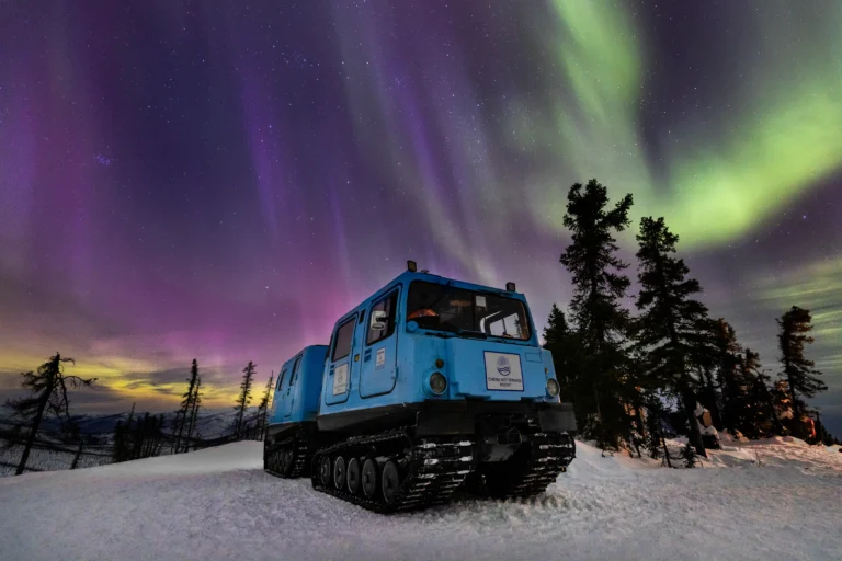 Tracked snow vehicle beneath colorful aurora skies at Chena