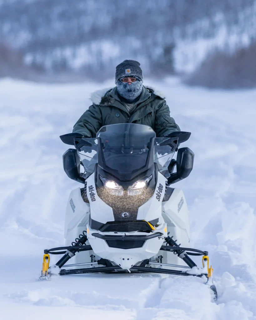 Close-up front view of an electric snowmobile with headlights on during a winter tour.