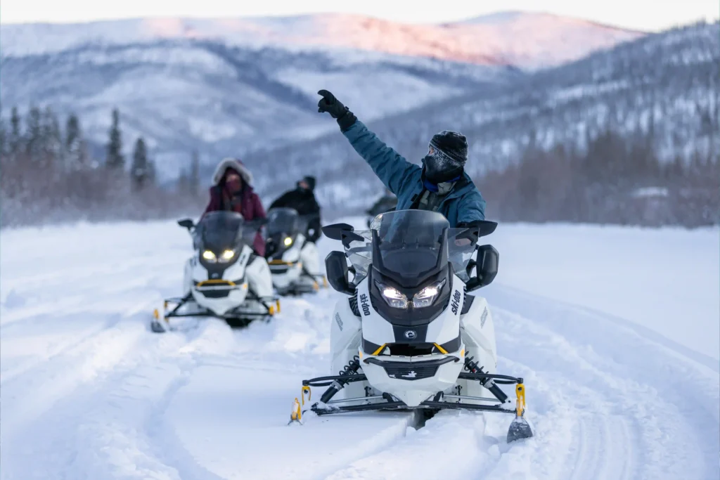 Two snowmobile riders pointing at the scenic mountain horizon during a snowmobile tour.