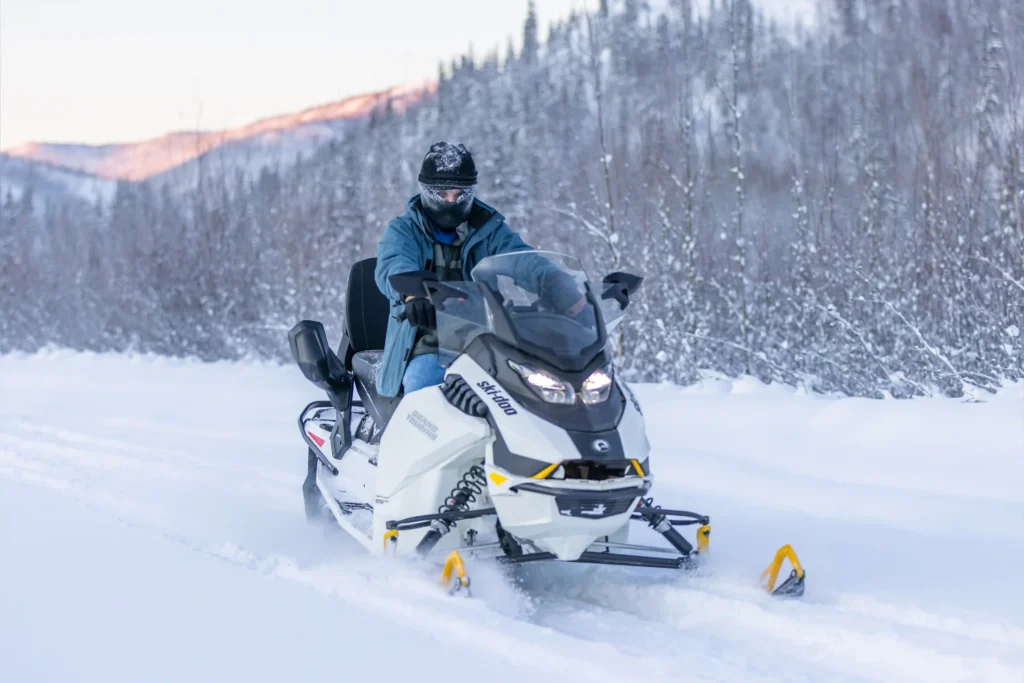Guest riding a white electric snowmobile through a scenic snow-covered Alaskan forest.