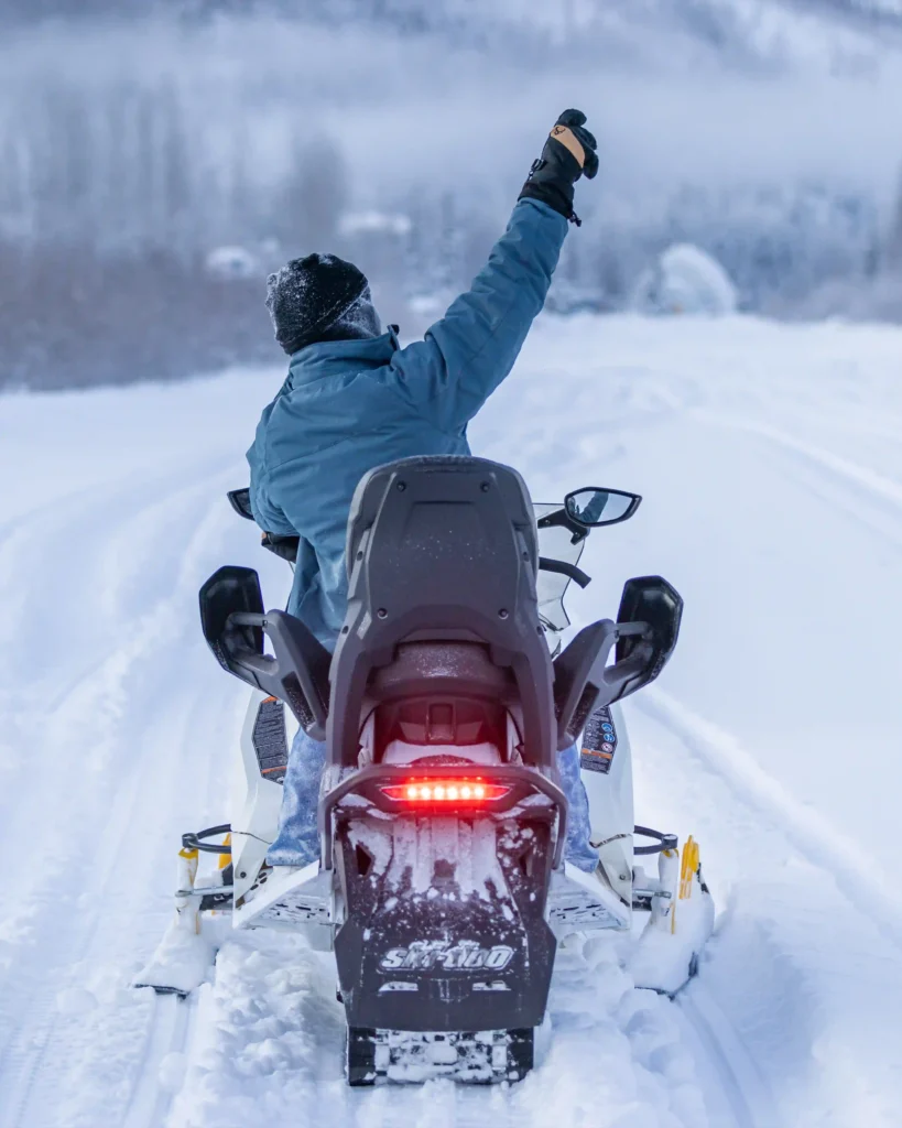 Rear view of a snowmobile rider waving while driving through deep Alaskan snow